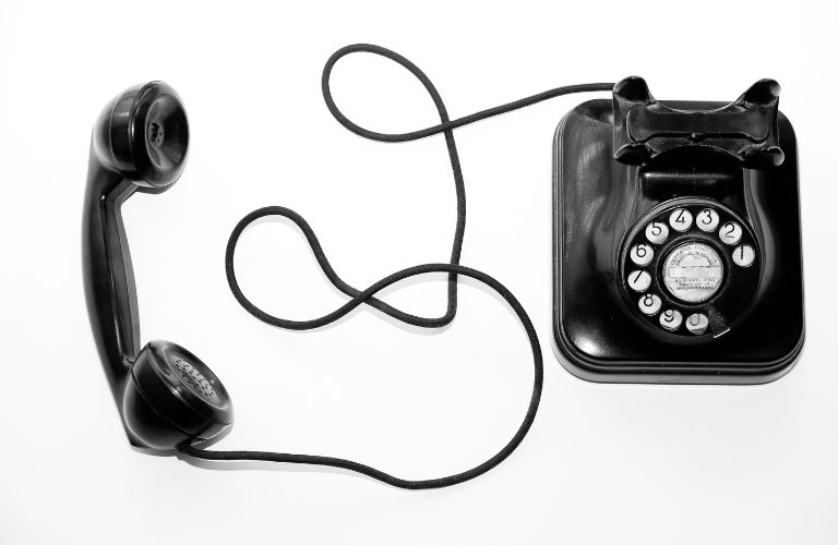 rotary phone off the hook black phone resting on white background