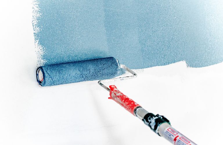 blue paint on paint roller with red handle being painted onto white wall