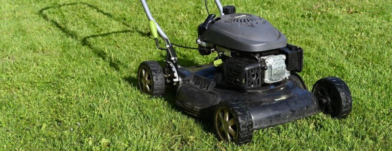 black lawn mower resting on green grass in the sunlight