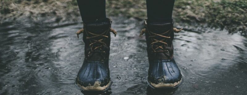 person with old black boots standing in a puddle in a field