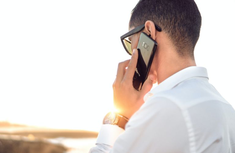 man on the phone looking into the sunset wearing sunglasses