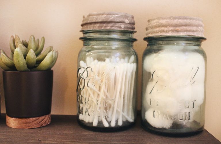cotton swabs and cotton balls stored in mason jars sitting on a table next to a small potted succulent
