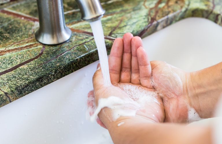 person washing hands with soap and aerated water at a kitchen sink with laminate countertop