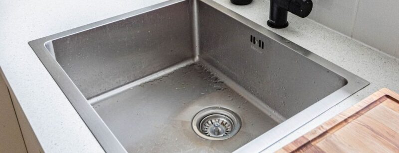 stainless steel kitchen sink empty and clean with dark faucet in corner