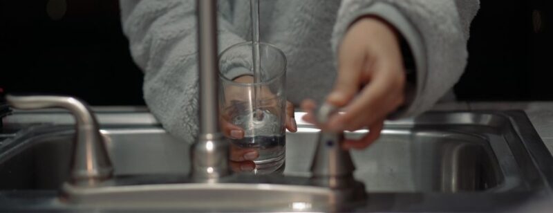 person filling up with water from kitchen sink wearing grey sweater