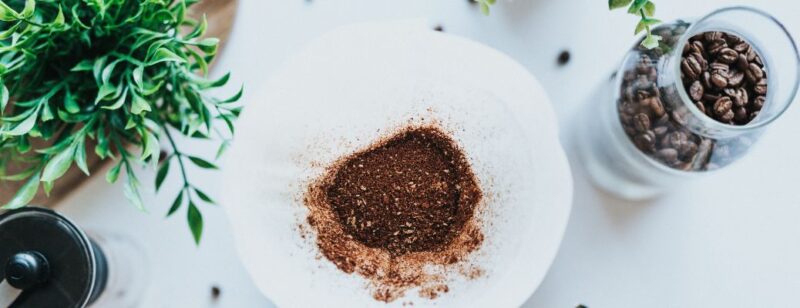coffee grounds in a coffee filter seen from above next to fresh coffee beans