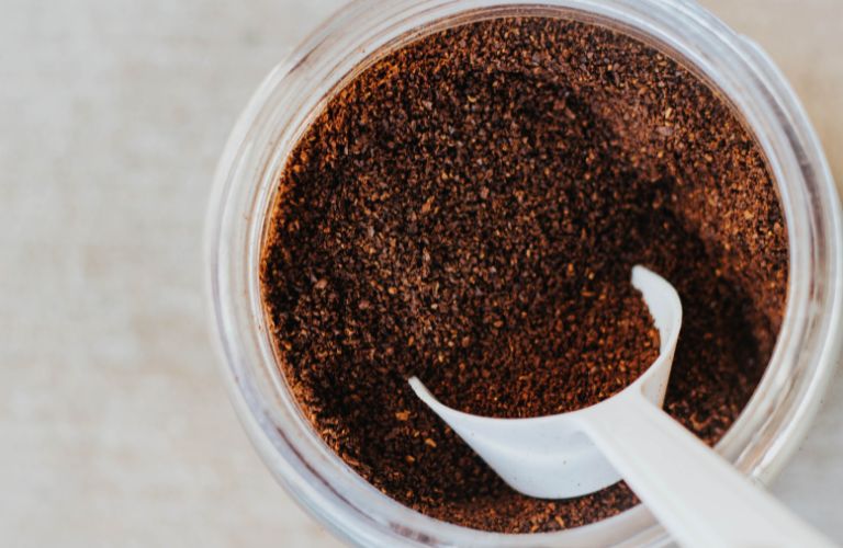 container of coffee grounds seen from above with a small plastic scoop sitting inside