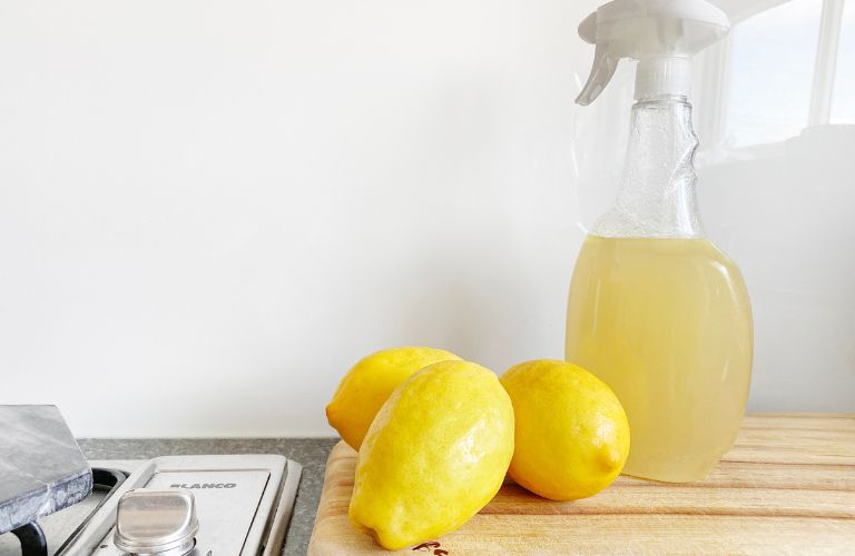 Lemon cleaner in spray bottle with lemons and countertop cutting board and stovetop
