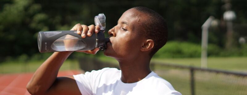 man drinking water from a water bottle and wearing a white shirt