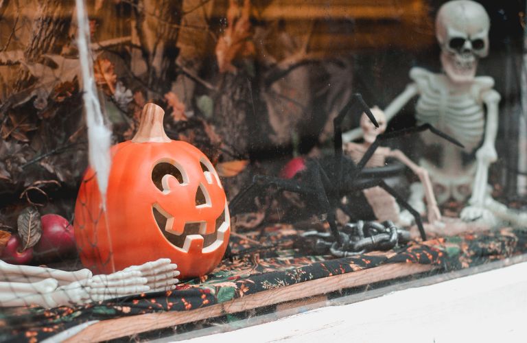window display of plastic skeletons pumpkin and spider for Halloween event storefront window netting