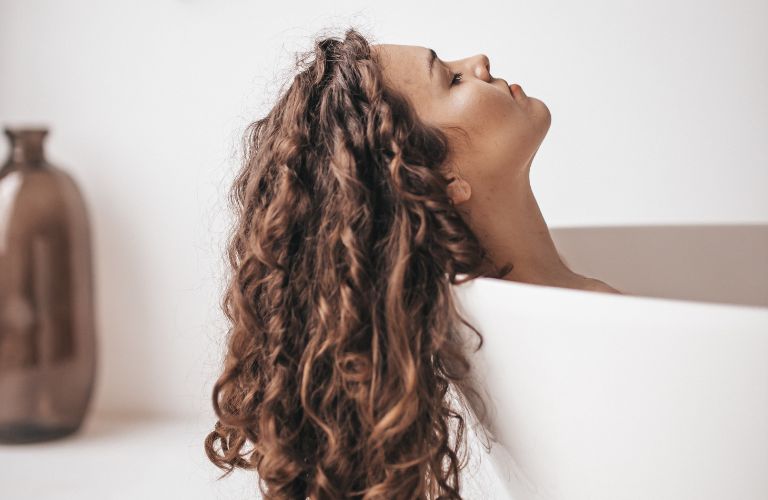 woman taking bath in tub with head on the edge and hair dry flowing over the edge