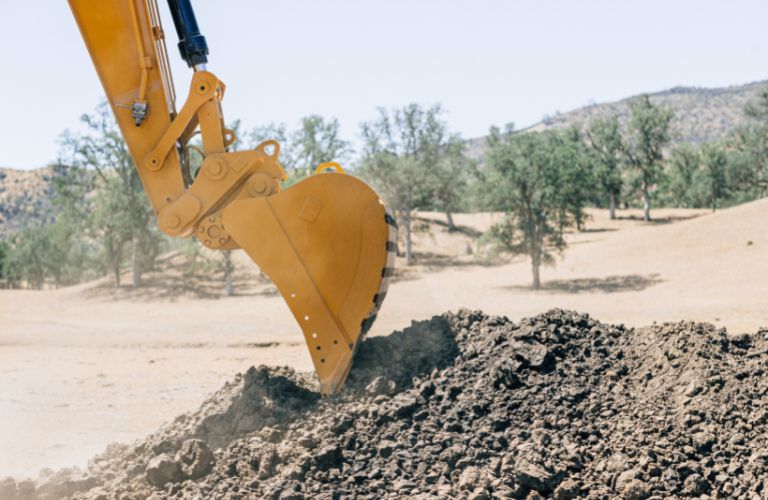 machine digging in the desert piling soil in the open digging a hole