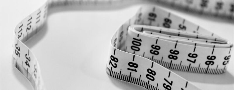 white measuring tape from a sewing kit sitting unraveled on a white table