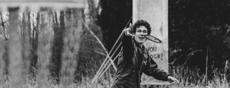 black and white photo of a young man throwing a frisbee at a disc golf basket