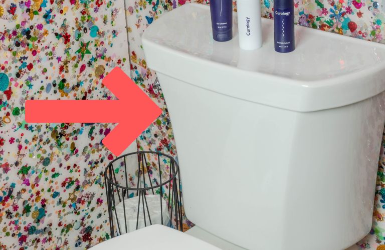 red arrow pointing at the tank of a toilet in a room with wallpaper