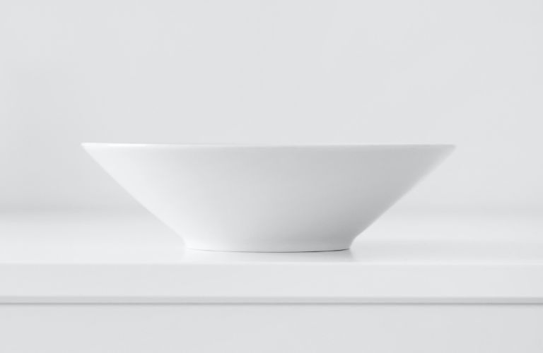 porcelain bowl plain white sitting on a white shelf against a white wall