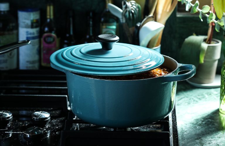 dutch oven ceramic cooking pot with lid slightly ajar and soup inside sitting on a stove