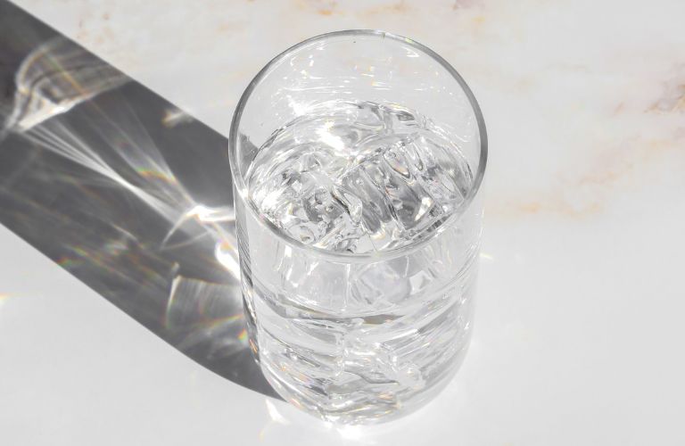 glass of water resting on a countertop with shadow and light going through it