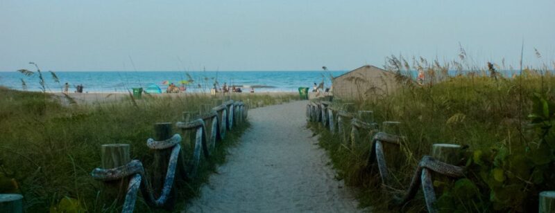 sandy trail to a beach between two fields of grass