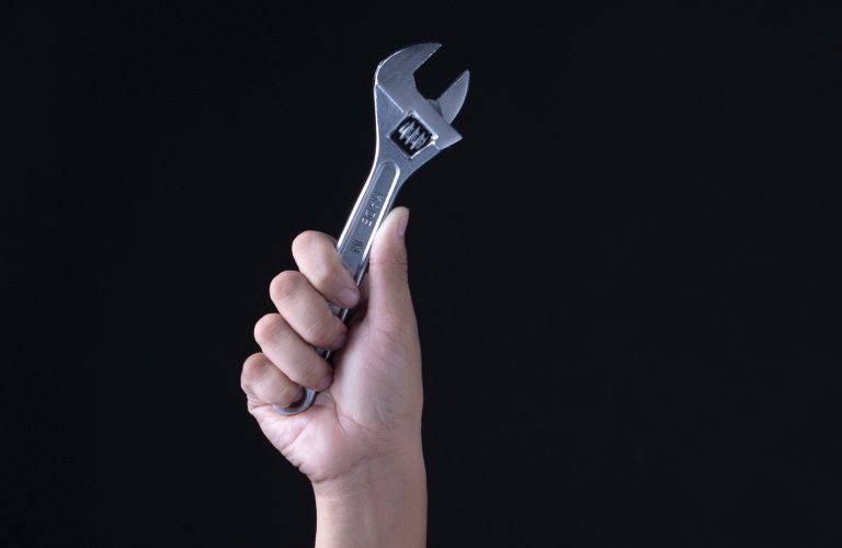 hand holding up crescent wrench against a black background