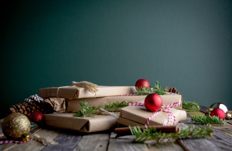 presents in brown paper with garland ornaments and pinecones on a wood table with a solid green background