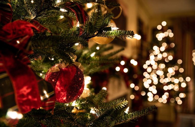 close up of Christmas tree lit up with white lights and red glass ornaments and ribbons