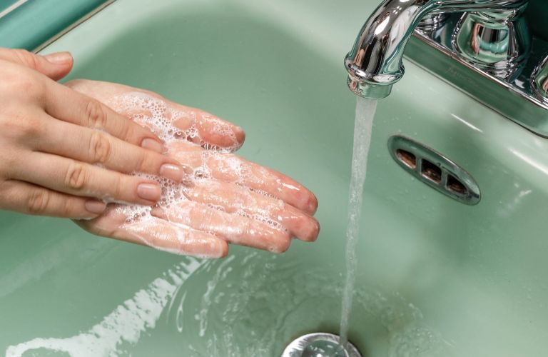 hands washing in a green bathroom sink with soap