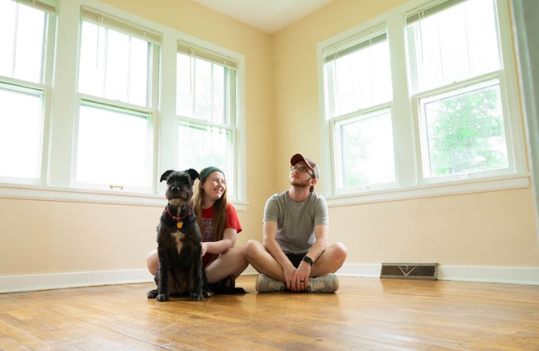 couple with a dog sitting in the front room of an empty house