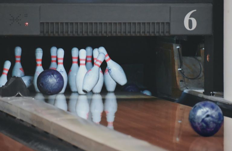 bowling balls rolling down a lane and hitting bowling pins