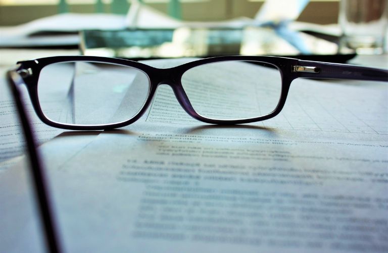 pair of reading glasses resting on a stack of papers