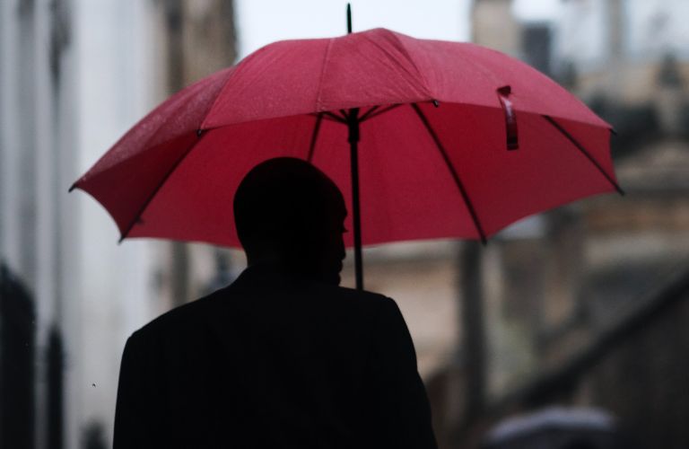 Man under umbrella in the rain walking down a city street