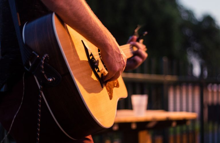 person playing acoustic guitar outdoors by a fence