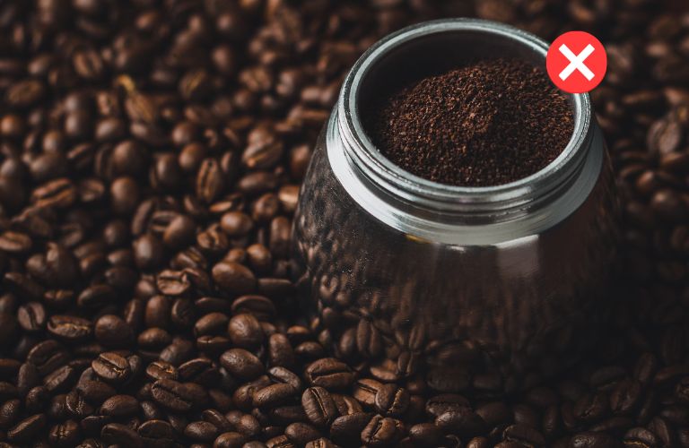 coffee grounds in a metal canister sitting on a mound of coffee beans