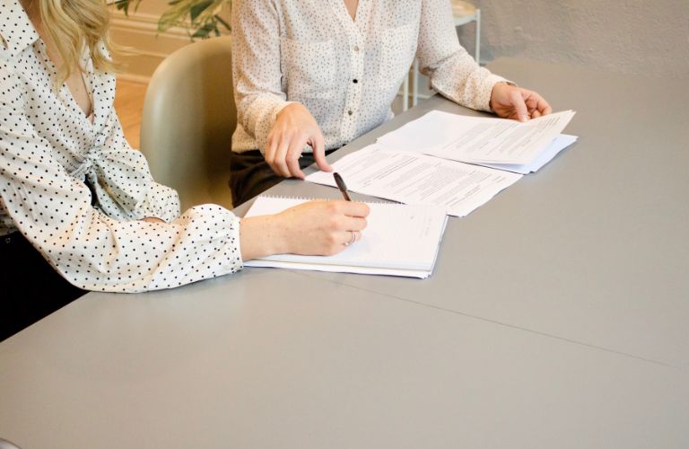 people signing documents on a white table while seated