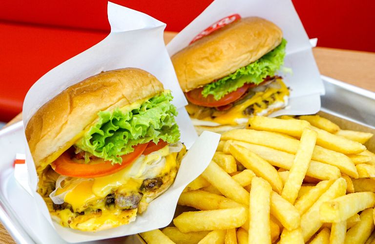 two burgers in paper next to a pile of french fries