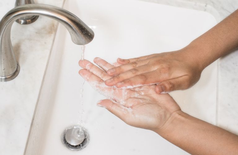 hands washing under a bathroom sink with suds and water