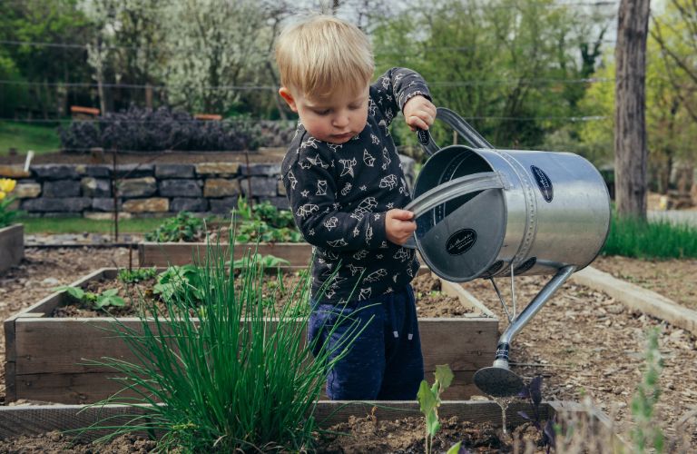 child watering a garden box with a metal watering can