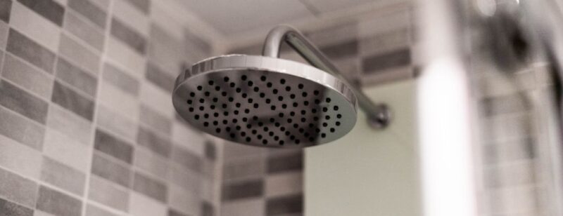 chrome shower head in a tile shower surround with no water