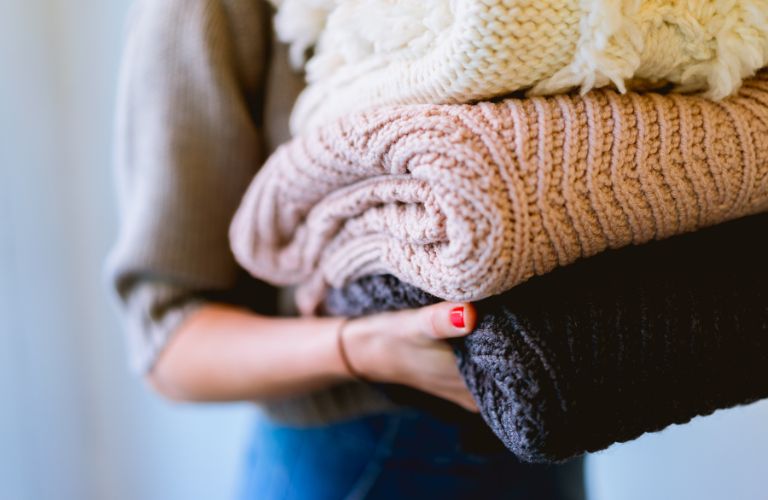 person holding a stack of folded sweaters