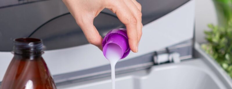 person pouring capfull of laundry liquid into a washing machine