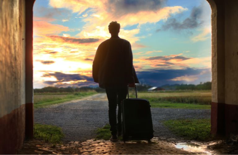 man wheeling luggage out of cobbled tunnel into open gravel road