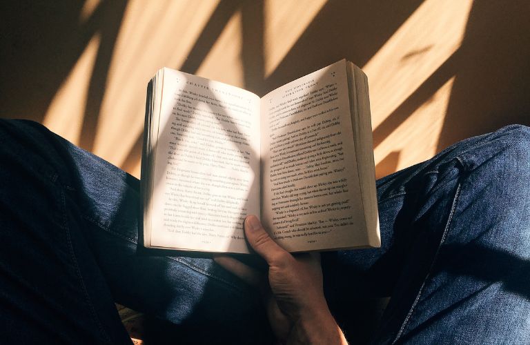 person sitting cross legged holding a book open reading