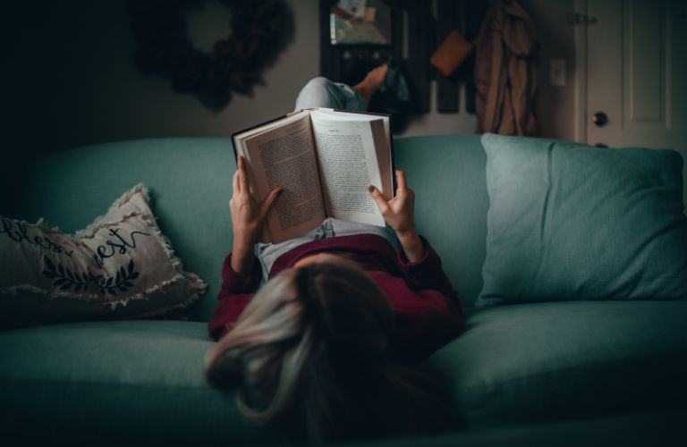 woman on a couch reading from a hardcover book