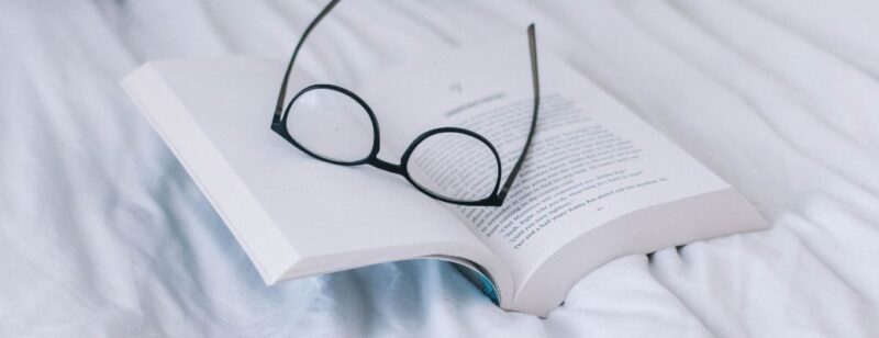 pair of reading glasses laying on an open book on top of a bed