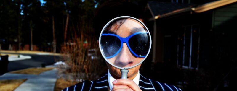 person with sunglasses looking through magnifying glass in search of something