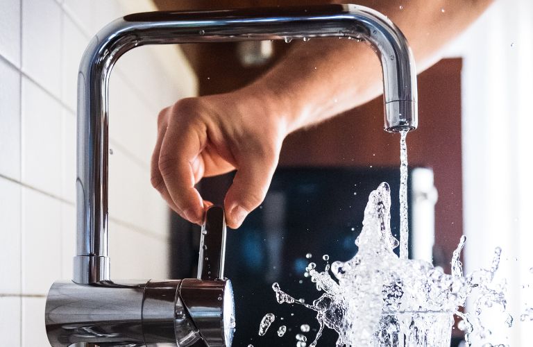 large steel faucet pouring water into a glass with a splash