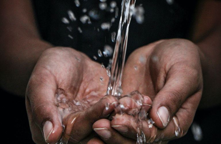 hands cupped to hold water pouring into them from a faucet