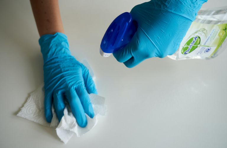 spray bottle of cleaning liquid being sprayed on a table and wiped with a paper towel