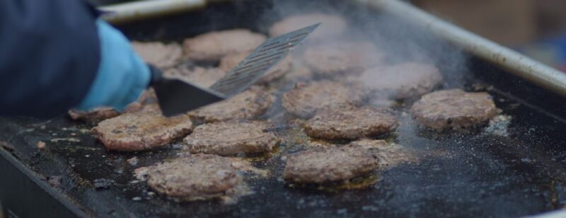 flat top grill where many hamburgers are being cooked in their own grease