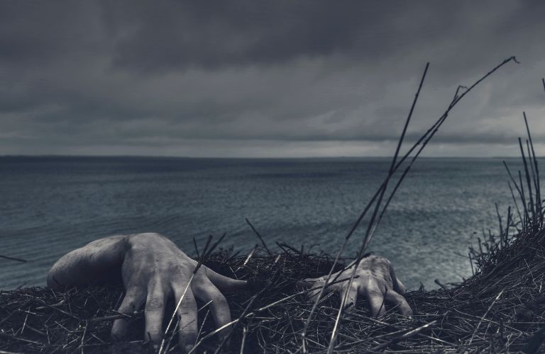 creepy pair of hands climbing up a grassy cliff edge near a shoreline